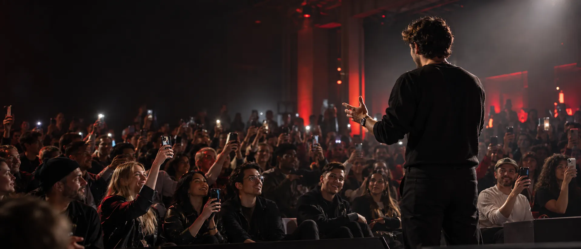 Creator on stage facing an audience holding smartphones under red lighting